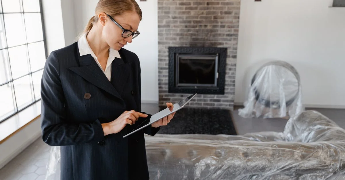 Une agente immobilière en costume utilise une tablette numérique pour examiner des documents dans un salon moderne.