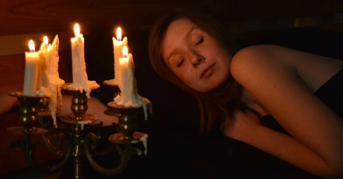 Une femme dort paisiblement à côté d'un chandelier avec des bougies allumées, créant une ambiance sereine.